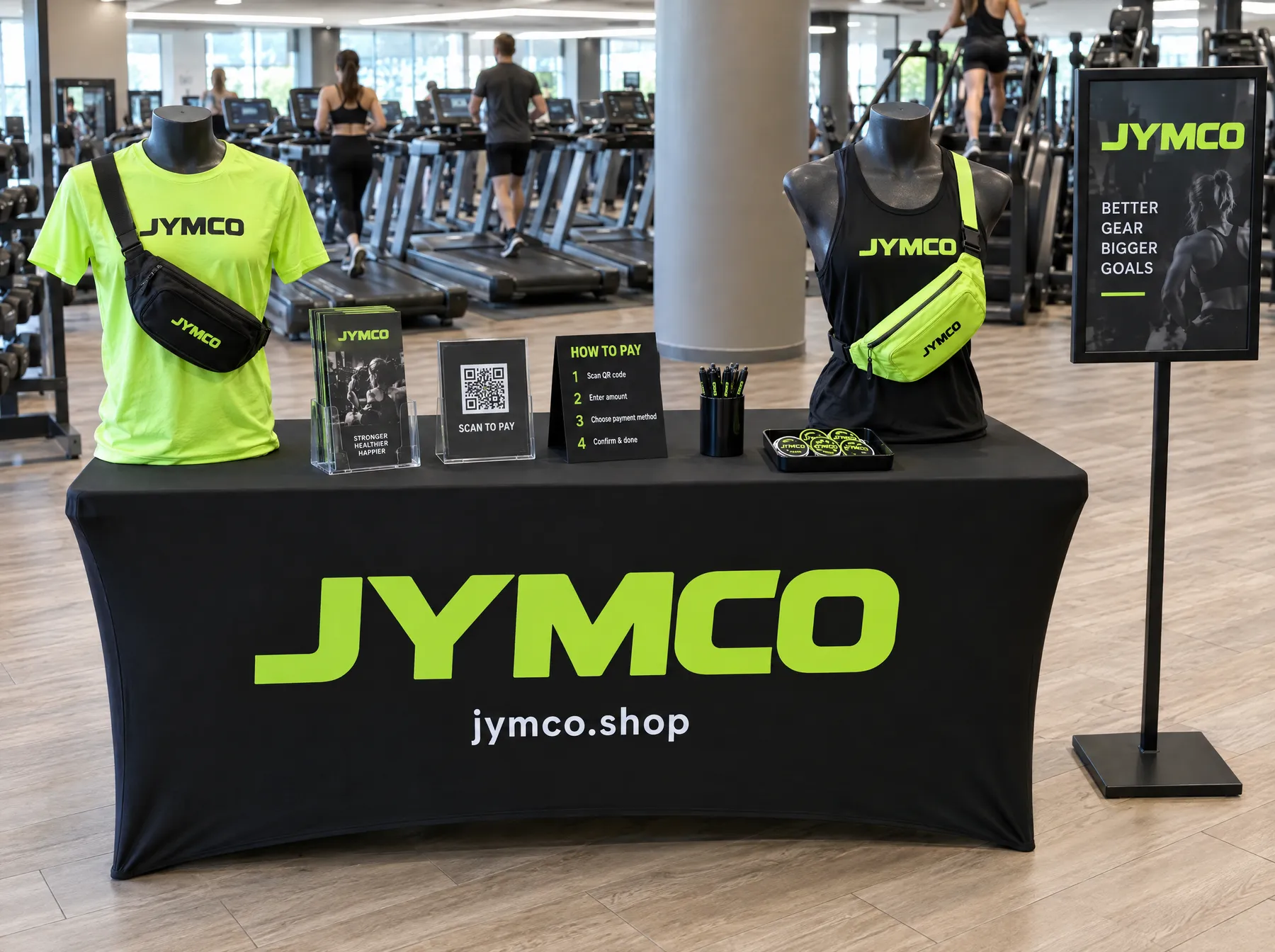 JYMCO booth table with a tee, tank, fanny packs, scan-to-pay QR sign and how-to-pay steps